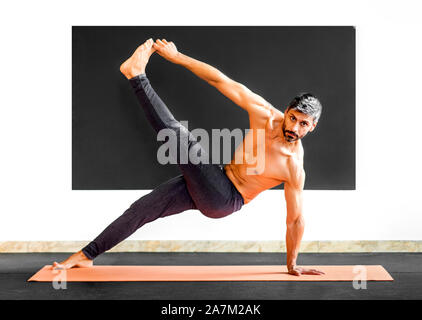 Man doing yoga stretch and balance exercises for mobility and strengthening his muscles in a gym in a health and fitness concept Stock Photo