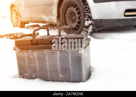 Car battery against the background of a car in winter. Winter battery discharge concept, copy space, charging the battery Stock Photo