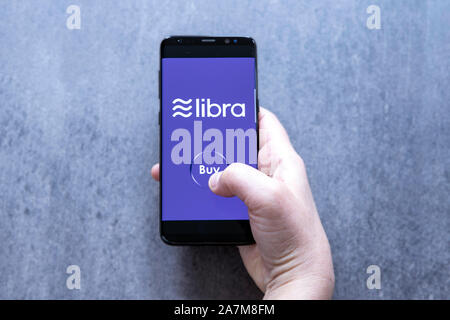 Hand holding smartfone with crypto currency logo Libra and buy button against gray blurred background. Stock Photo