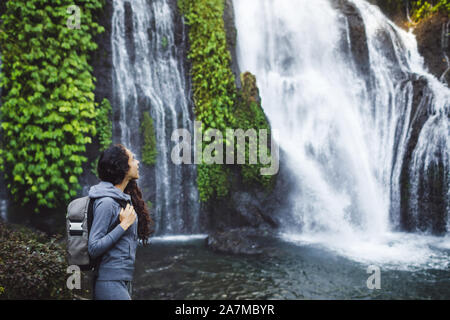 Woman watching waterfall Banyumala in Bali. Long curly brunette hair, backpack. Travel concept. Stock Photo
