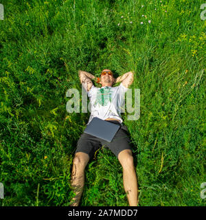 Top view of man lying down on grass with laptop Stock Photo