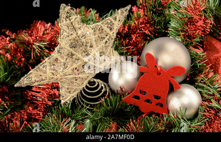 Background for Christmas greeting composed of golden thread star, red flieltro bell and gray balls on red and green tinsel bed on black background Stock Photo
