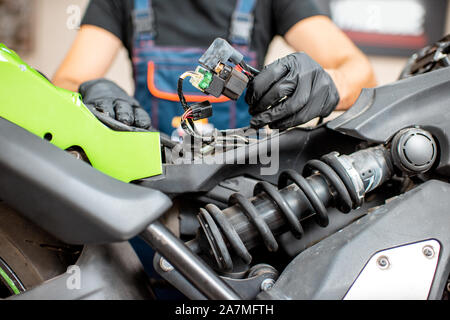 Electrician or repairman in protective gloves connecting wiring in the motorcycle during a repairment at the workshop Stock Photo