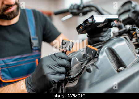 Electrician or repairman in protective gloves connecting wiring in the motorcycle during a repairment at the workshop Stock Photo