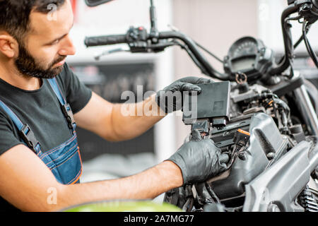 Electrician or repairman in protective gloves connecting wiring in the motorcycle during a repairment at the workshop Stock Photo
