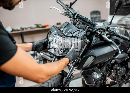 Worker removing broken headlight after the accident, repairing motocycle in the workshop, close-up view Stock Photo