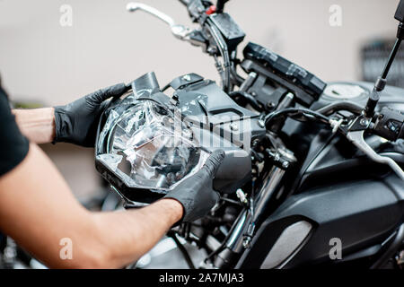 Worker removing broken headlight after the accident, repairing motocycle in the workshop, close-up view Stock Photo