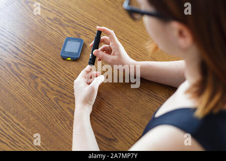 Woman using lancet to take blood sample to check glucose level with traditional glucometer Stock Photo