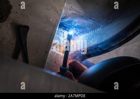 Man with a helmet and no gloves welds in the metal of a car and repairs a rusty hole Stock Photo