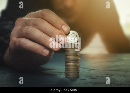 Man putting a coin with the word liberty on a money stack. Finance, banking, savings, personal budget, liberalism, increase in wealth concepts. Stock Photo