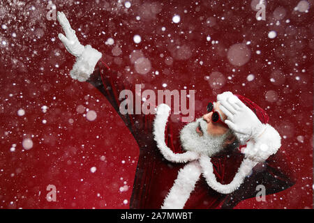 Waist up portrait of funky Santa dancing over red background with snow falling, copy space Stock Photo