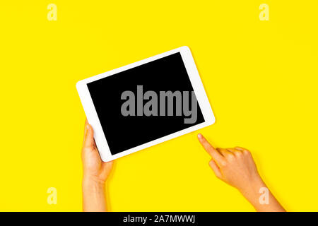 Kid hand holding white tablet computer and pointing to blank screen on yellow background Stock Photo