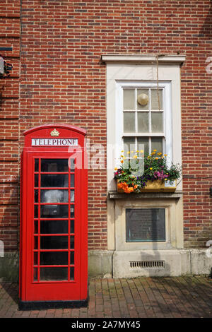 Iconic red British telephone box in front of a brick building with window and flower box on a bright, sunny day, Sidmouth, Devon, UK