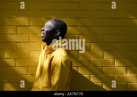 African Young Man Smiling With Yellow Wall In Background Stock Photo
