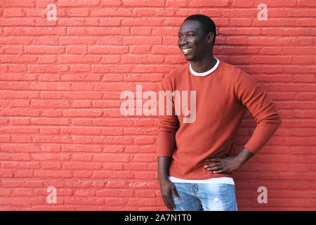 African Young Man Smiling And Leaning On Red Wall Stock Photo