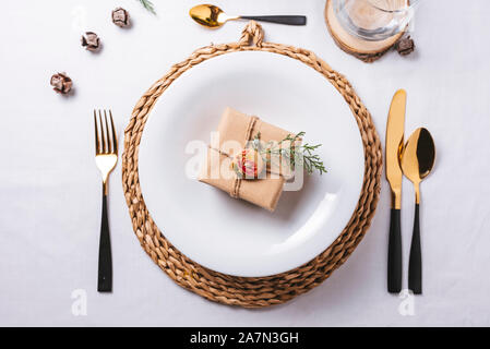 Elegant Christmas place settings with gold and white decoration and golden cutlery. gift box on the dish from above Stock Photo