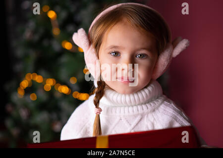 Beautiful little girl in the hat sitting near presents and christmas tree. Bokeh lights on the background. Concept christmas and new year Stock Photo