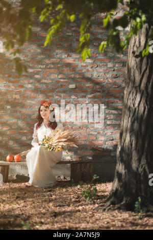 Young woman in traditional white dress sitting on bench by the old house Stock Photo