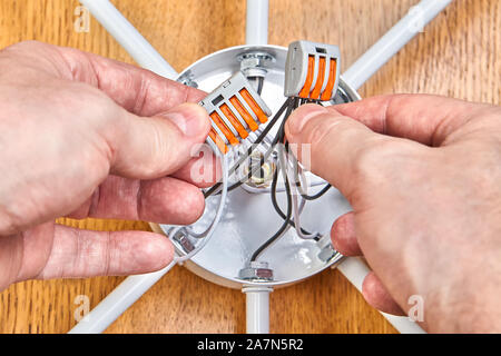 An electrician mounts the wiring inside the electrical box of the ceiling lamp using a terminal block with levers and spring clips. Installation of a