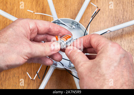 Splicing electric wires in a electrical box of a ceiling chandelier using a spring-loaded lever terminal block. An electrician mounts a wiring of a li