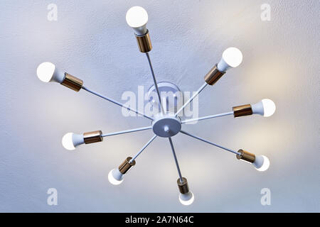 Ceiling light, white painted aluminum chandelier with eight led bulbs. Household lighting fixture with 8 ray tubes for electric lamps. Stock Photo