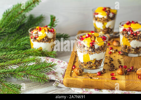 Greek yogurt with granola, orange and pomegranate berries for healthy breakfast on wooden board, New Year or Christmas food still life copy space, sha Stock Photo