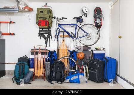 Sports and travel gear and equipment in piles in corner of messy suburban garage. Stock Photo