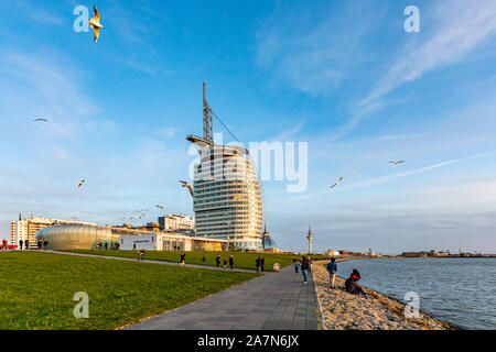 Bremerhaven, Germany - 2 Nov 2019: People playing with seagulls on Weser river Promenade am Strom riverfront embarkment in sunset. Sail-shaped Atlanti Stock Photo