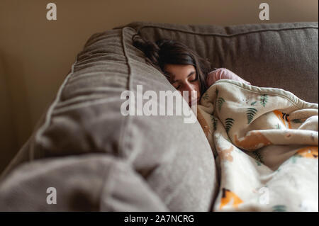 Tween girl 10-12 snuggled up sleeping in corner of couch at home Stock Photo