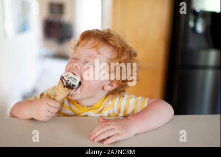 Toddler taking a big bite of his ice cream come at home in kitchen Stock Photo