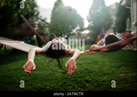 Brother and sister relaxing in hammock together in backyard Stock Photo