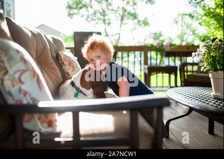 Toddler boy hugging his basset hound dog on the deck in spring Stock Photo
