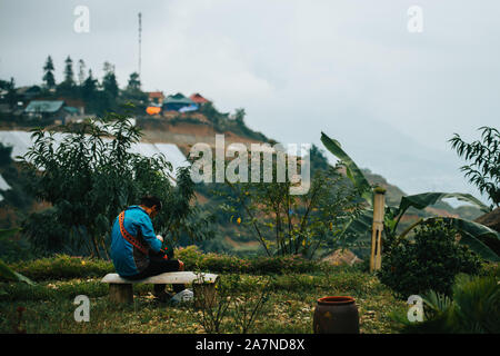 A local Vietnamese woman makes clothes surrounded by rice terraces in the small mountain town Sapa in the Northern mountains of Indochina Stock Photo
