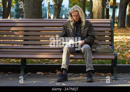 Kharkiv, Ukraine - October 14, 2019: The guy sits on a bench in the autumn park and reads book Stock Photo
