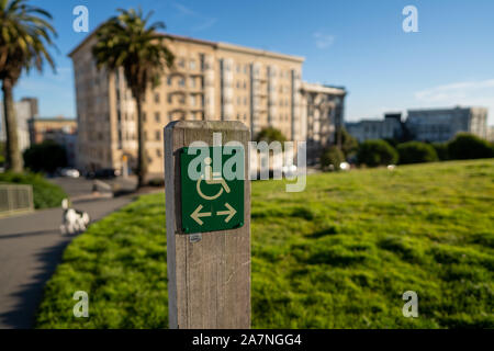 Handicap logo wheelchair on wooden post in city park with arrows pointing left and right Stock Photo