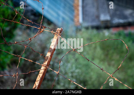 Top of rusty fence with barbed wire protecting wooden area Stock Photo