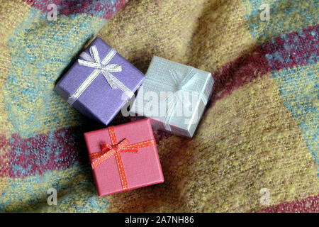 Three holiday gifts in small colored boxes, covered with ribbon with bows, against a background of woolen fabric top view close-up Stock Photo