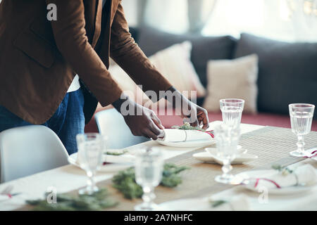 Cropped portrait of young African-American man preparing table setting while decorating dining room for Christmas party at home, copy space Stock Photo