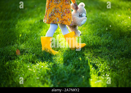 Little girl hugging toy teddy bear in autumn park. Playing with fallen leaves. Stock Photo