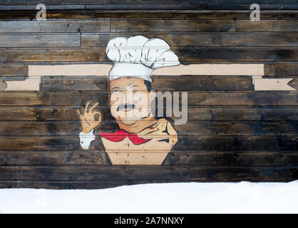 Wooden wall with graffiti style painting of retro cartoon chef wearing hat and pointing with right hand that everything is fine Stock Photo
