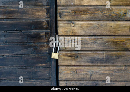 Close-up view of a locked padlock on a varnished brown pine wooden back door. Stock Photo