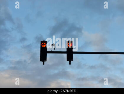 Low angle view of red  traffic lights   with the arrow pointing to ahead  and the left against cloudy blue  sky at sunset . Stock Photo