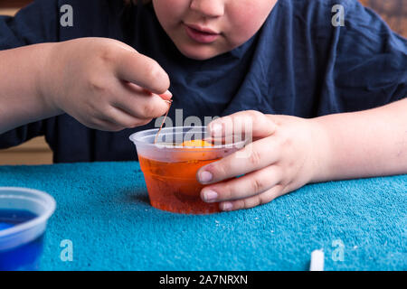 Child inspecting a colored egg to see if it is done being dyed at easter Stock Photo