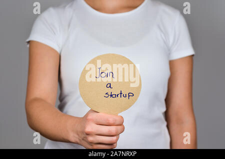 Young women  showing   round cardboard paper     with handwritten blue  text  - Join a Startup. Stock Photo