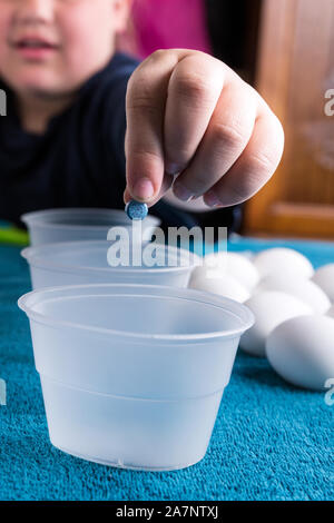 Child dropping coloring tablet into vinegar for easter egg dyeing Stock Photo