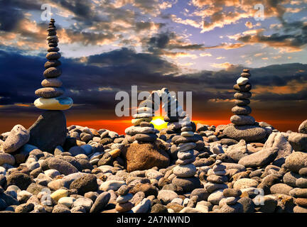 Stacked stones on the beach at sunset. Sunlight between the stones. Stones pyramid, zen concept. Stock Photo