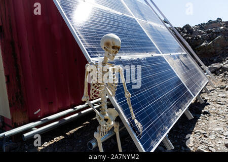 Skeleton leaning on solar panels in the desert Stock Photo