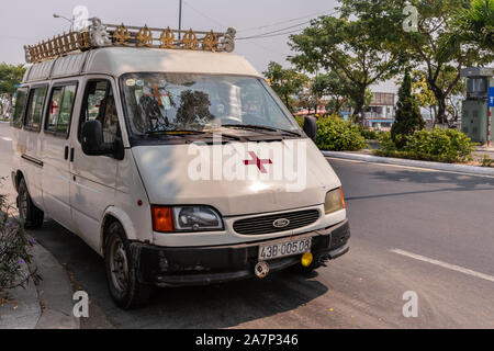 Da Nang, Vietnam - March 10, 2019: White ambulance van with red cross on wide road with green foliage. Stock Photo