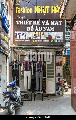 Da Nang, Vietnam - March 10, 2019: Display of pants and shirts for men outside fashion store with giant billboard above entrance and motorcycles aroun Stock Photo