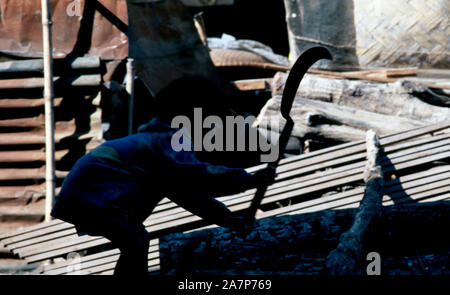 A young, indigenous Mnong (Pnong) girl chopping firewood in her village in Sen Monorom, Cambodia. Stock Photo